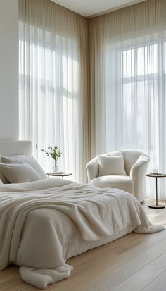 a white bed sitting in a bedroom next to two chairs and a window with sheer curtains