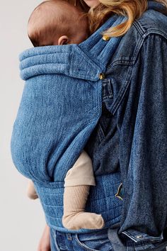 a woman holding a baby in a denim carrier