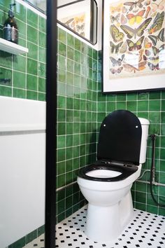 a black and white toilet sitting in a bathroom next to a green tiled wall with pictures above it