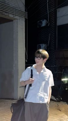 a young man with glasses is walking down the street carrying a bag and looking at his cell phone