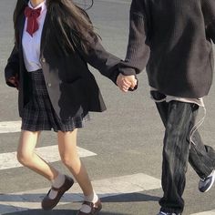 a man and woman walking across a cross walk holding hands, both wearing school uniforms