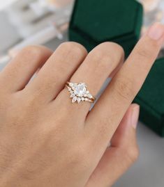 a person's hand holding a ring with three stones on it and two green velvet boxes in the background