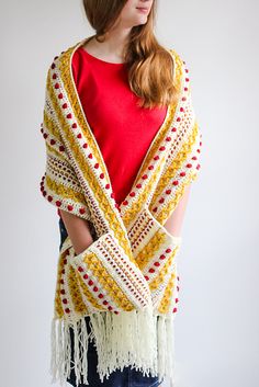 a woman wearing a yellow and white crocheted shawl with fringes on it