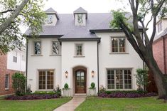 a white house with two story windows and trees in the front yard, surrounded by green grass