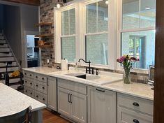 a kitchen with white cabinets and marble counter tops, along with stairs leading up to the second floor