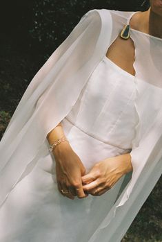 a woman in a white dress is holding her hands together