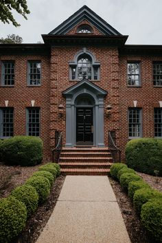 a large brick building with steps leading up to the front door and green bushes on either side