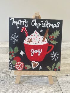 a christmas card with a cup of hot chocolate and candy canes in it on an easel