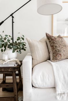 a living room with white couches, pillows and a lamp on the side table