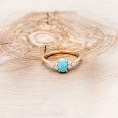 a gold ring with a turquoise stone surrounded by white diamonds on a tree stump background