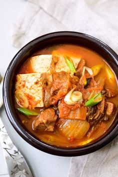 a bowl filled with stew and tofu on top of a white cloth next to a spoon