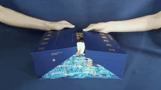 two hands reaching out to open a blue box with an image of a pyramid on it