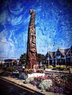 a large wooden statue sitting on the side of a road next to flowers and trees