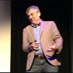 an older man is standing on stage with his hands in his pockets and holding a cell phone