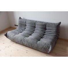 a grey futon couch sitting on top of a wooden floor next to a wall