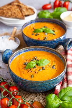 two blue bowls filled with soup next to bread and tomatoes