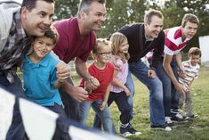 a group of men and children playing frisbee in the grass with each other