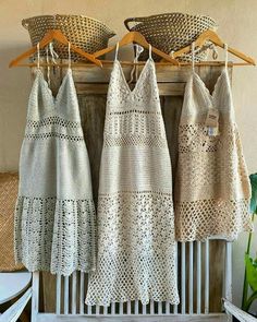 three crocheted dresses hanging on a rack in front of a basket and plant