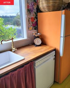 a kitchen with an orange refrigerator next to a white sink and dishwasher in front of a window