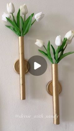 two vases with white flowers are on the wall and one has green leaves in it