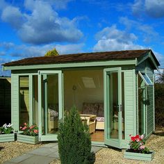 a small green shed sitting on top of a gravel field next to a lush green bush