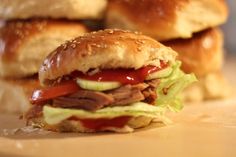 two sandwiches with meat, lettuce and tomato on them sitting on a cutting board