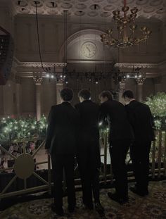 three men in suits stand at the top of a balcony looking out onto an indoor christmas tree