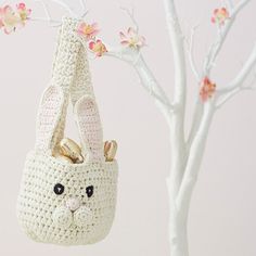 a crocheted bunny bag hanging from a tree with pink flowers in the background