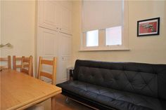 a black leather couch sitting in front of a wooden dining table with chairs around it