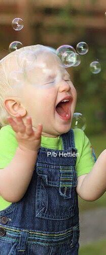 a toddler playing with soap bubbles in the air while wearing overalls and green t - shirt