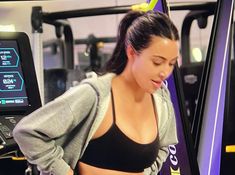 a woman in a sports bra is looking at her cell phone while standing on a tread machine