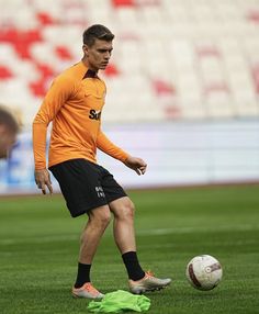 a man in an orange shirt is kicking a soccer ball on the field with green socks