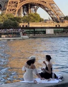 two women sitting by the water in front of the eiffel tower