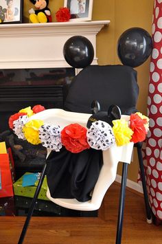 a mickey mouse chair decorated with paper flowers and black balloons in front of a fireplace