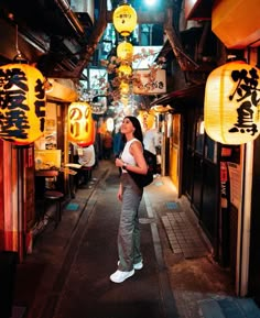 a woman standing in an alley with lanterns hanging from the ceiling