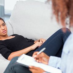 a woman sitting on a couch with a notepad in her hand and another person writing