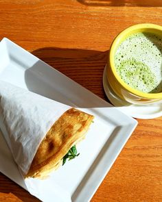 a burrito sitting on top of a white plate next to a cup of green tea