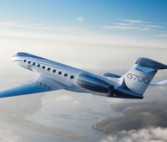 a blue and white airplane flying over the clouds in the sky with water below it