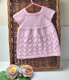 a pink knitted sweater sitting on top of a wicker basket next to flowers