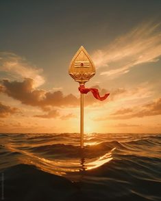 the sun is setting over the ocean with a pole in the water that has a red ribbon on it