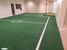 an indoor basketball court with green grass and white lines on the floor, in a basement