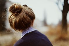 a woman's hair in a bun is seen from the back, with trees in the background