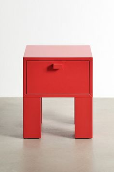 a small red table sitting on top of a cement floor next to a white wall