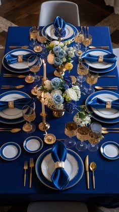 the table is set with blue and white plates, silverware, and gold place settings