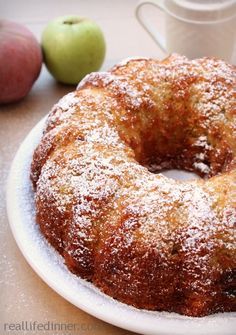 a cake sitting on top of a white plate next to two apples and a cup