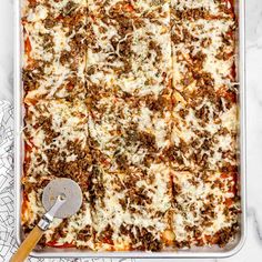 a square casserole dish with meat and cheese on top, next to a spatula