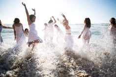 a group of young women splashing in the water at the beach on a sunny day