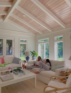 two people sitting on couches in a living room with large windows and wooden ceiling beams