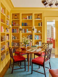 a dining room with yellow bookcases and red chairs in the center, on instagram