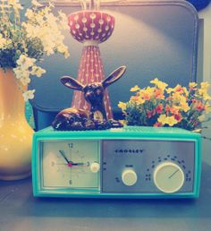 a clock sitting on top of a radio next to flowers and a vase with an antelope